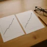 Zwei ausgedruckte Kursverläufe nebeneinander auf einem Schreibtisch, nahezu deckungsgleich